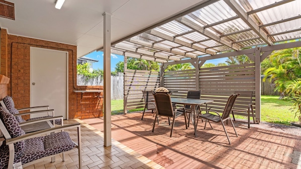 A covered patio with a table and chairs, a grill, and a brick wall.