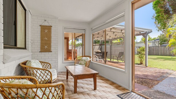 Un patio iluminado por el sol con muebles de mimbre, una mesa de madera y vistas al jardín trasero.