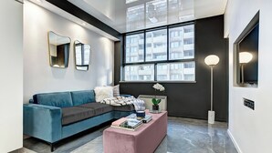 Un soggiorno moderno con un divano blu, un poggiapiedi rosa e un'ampia finestra vista edifici.