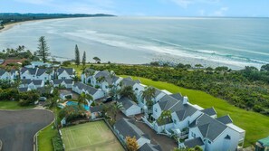 A coastal resort with multiple-story buildings, a tennis court, and a pool.