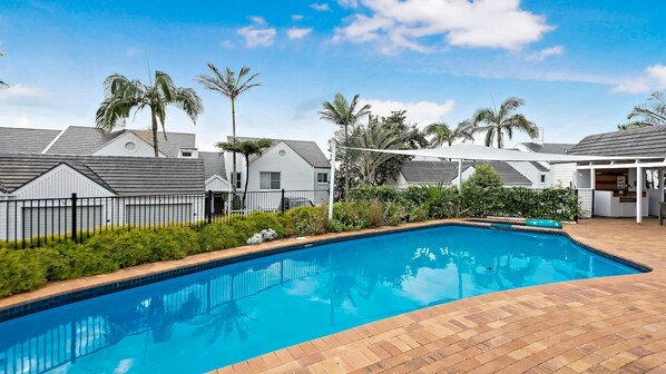 A swimming pool with a brick deck, surrounded by a fence and palm trees.