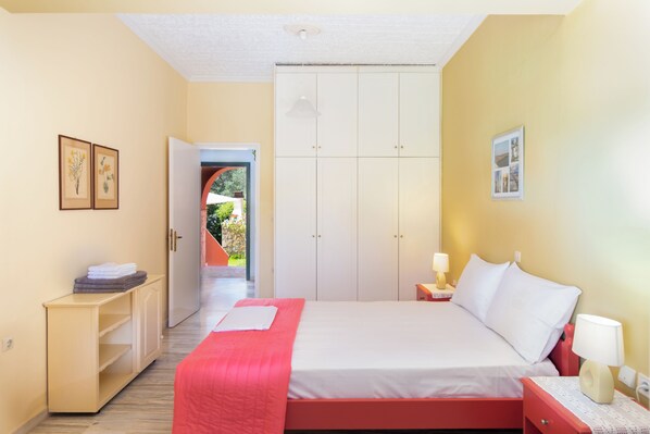 Een slaapkamer met een bed, nachtkastje, lamp, kledingkast en een deur naar een balkon.