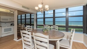 A dining area with a large table, white chairs, and a view of the ocean through large windows.