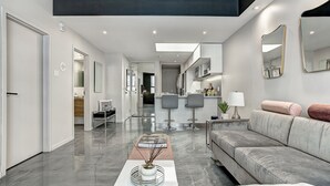 Ein modernes Wohnzimmer mit grauem Sofa, einem Couchtisch und einem Essbereich mit zwei Barhocker.