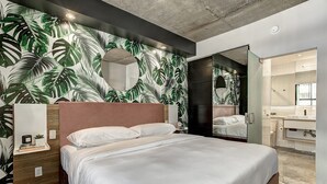 Ein modernes Schlafzimmer mit einem großen Bett, einem Nachttisch aus Holz, einem Spiegel und einem durchgegangene Tür erkennbaren Badezimmer.