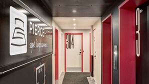 Ein Hotelgang mit modernem Design, mit einer Rezeption mit Logo, einer Tür mit der Nummer 304 und roten sowie schwarzen Dekorationselementen.