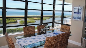 A dining area with a view of the ocean, wicker chairs, a glass table, and a decorative fish sculpture.