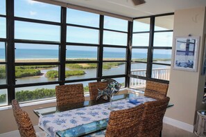 A dining area with a view of the ocean, wicker chairs, a glass table, and a decorative fish sculpture.