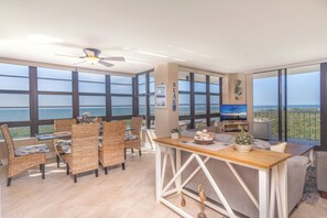 A spacious room with large windows, wicker furniture, a wooden table, and a television. - Beachfront unit with southwest to northwest exposures. South Seas Tower 4- 1212 (Marco Island)