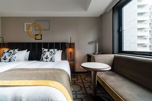 Habitación de hotel con una cama grande, un sofá, una mesita y una ventana con vista a un edificio.