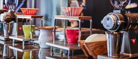 Una cafetera con un molinillo y un filtro de café, con una taza roja y una taza verde sobre la encimera.