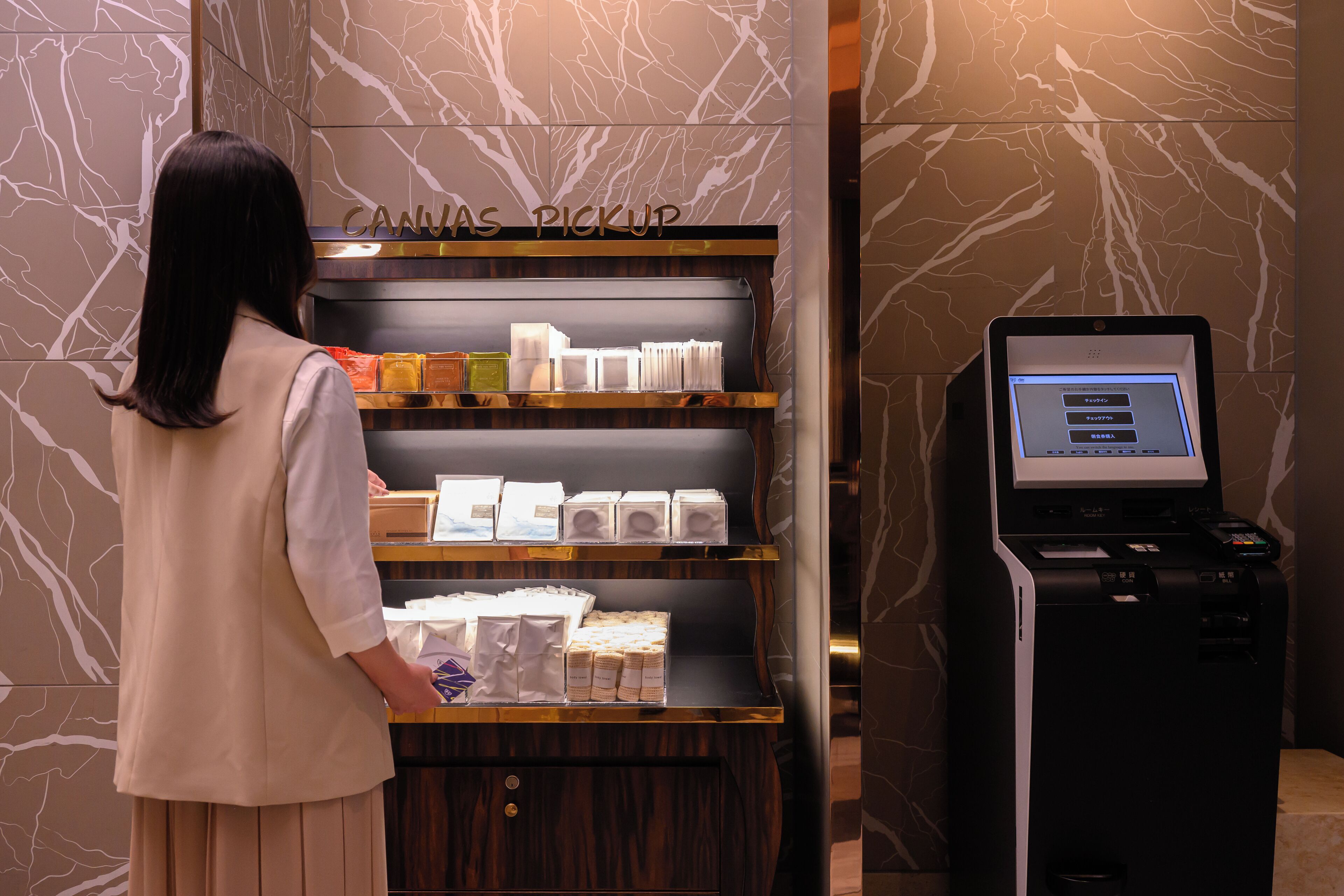 A woman standing at a self-service kiosk labeled "CANVAS PICKUP" with a selection of items on display.