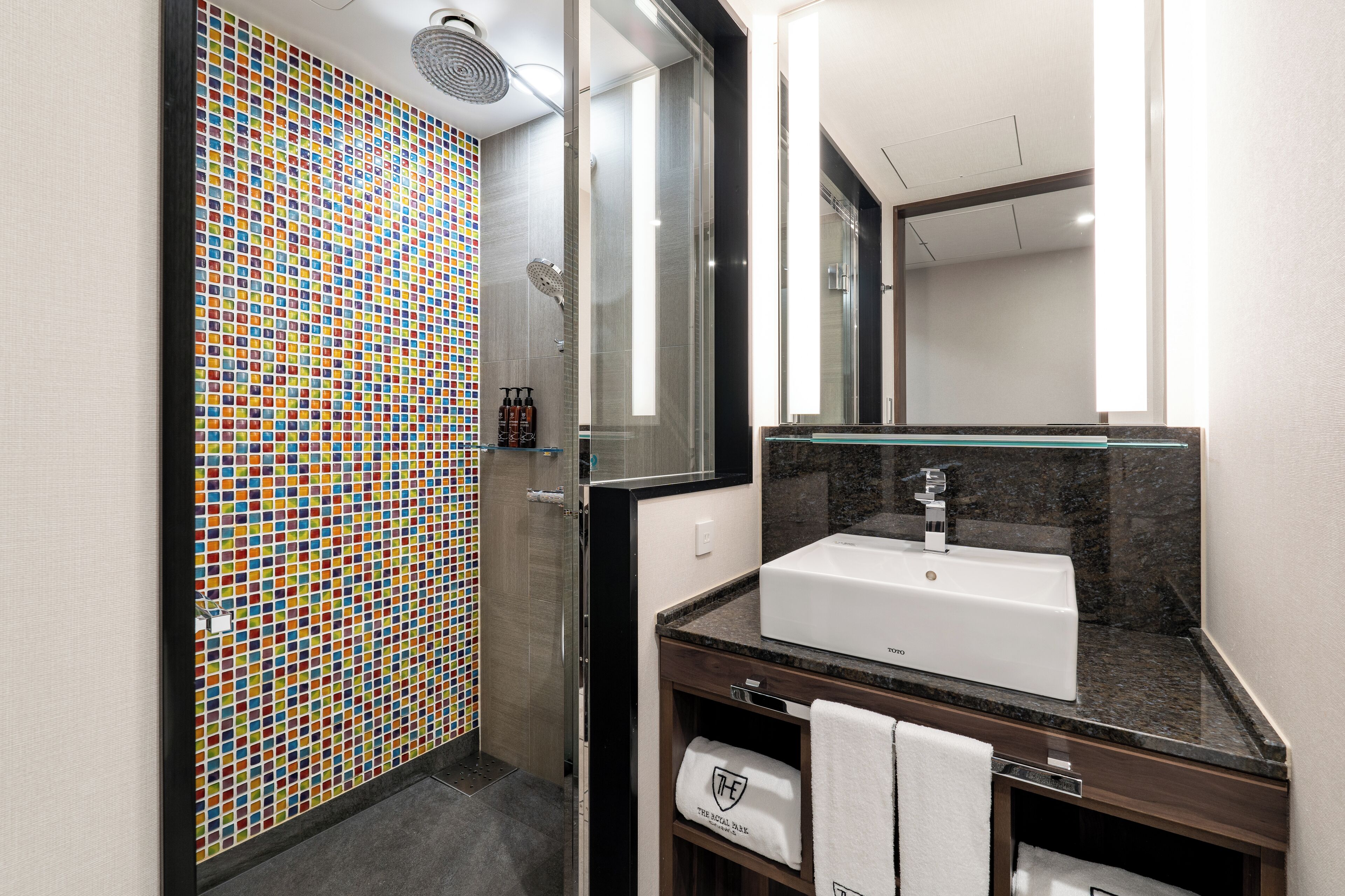 A modern bathroom with a tiled shower wall, a white sink, and a mirror.
