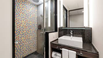 A modern bathroom with a tiled shower wall, a white sink, and a mirror.