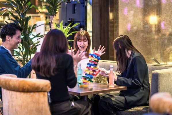Un groupe de personnes est assis autour d’une table, devant une pile de blocs de couleurs vives, une bouteille d’eau et une bouteille de soda.