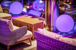 Un espacio lounge moderno con mobiliario de mimbre, una mesita de madera e iluminación ambiental.