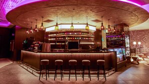 Un espace bar doté d’un comptoir incurvé, de plusieurs suspensions décoratives et de tabourets de bar.
