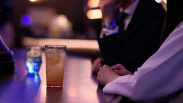 A bar setting with a glass of drink and a person seated at the bar.
