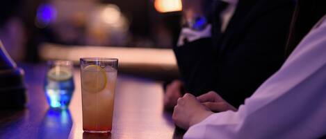A bar setting with a glass of drink and a person seated at the bar.