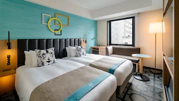 A hotel room with two beds, a round table, a bench, a lamp, and a window with a city view.
