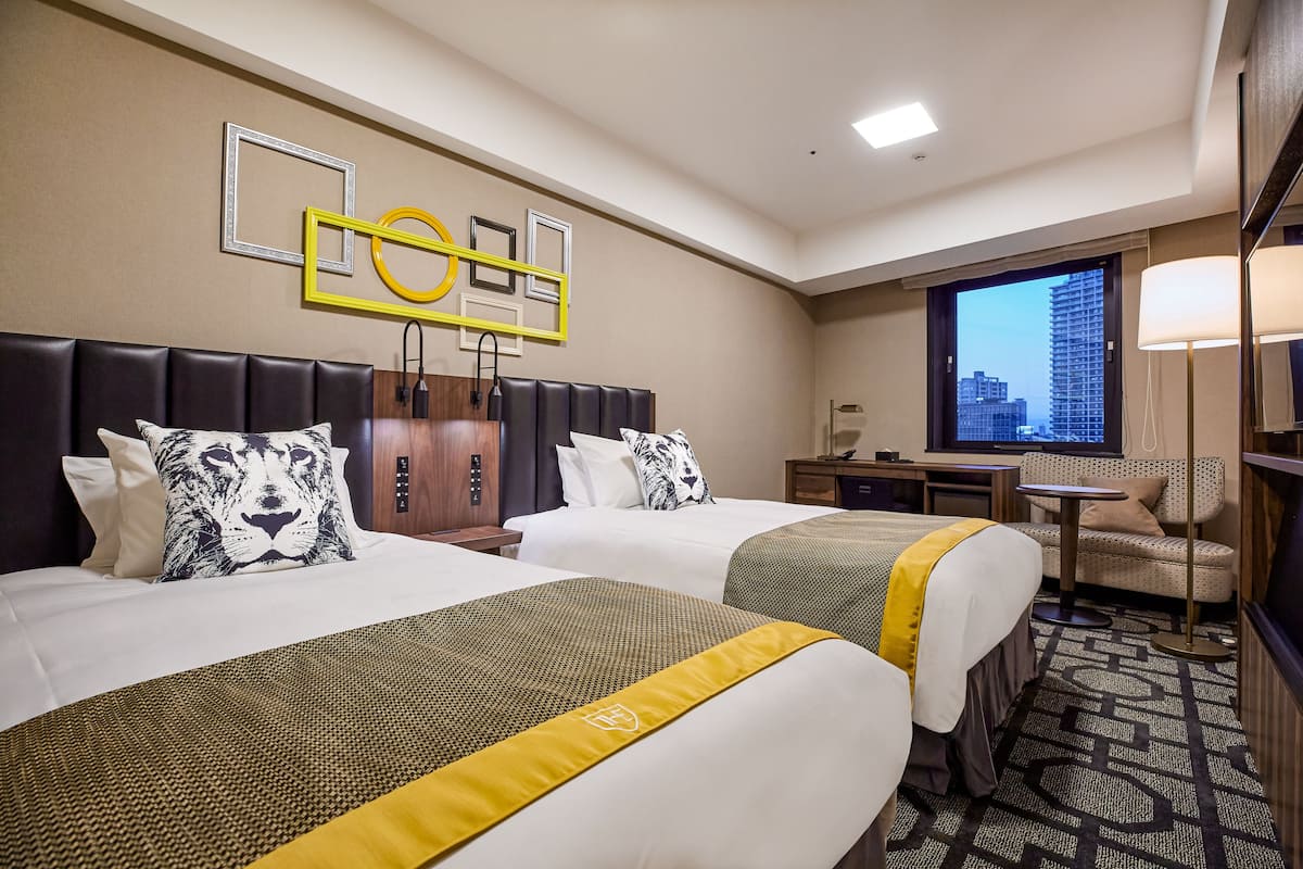 Une chambre d’hôtel avec deux lits, un bureau, une chaise et une grande fenêtre donnant sur la ville.