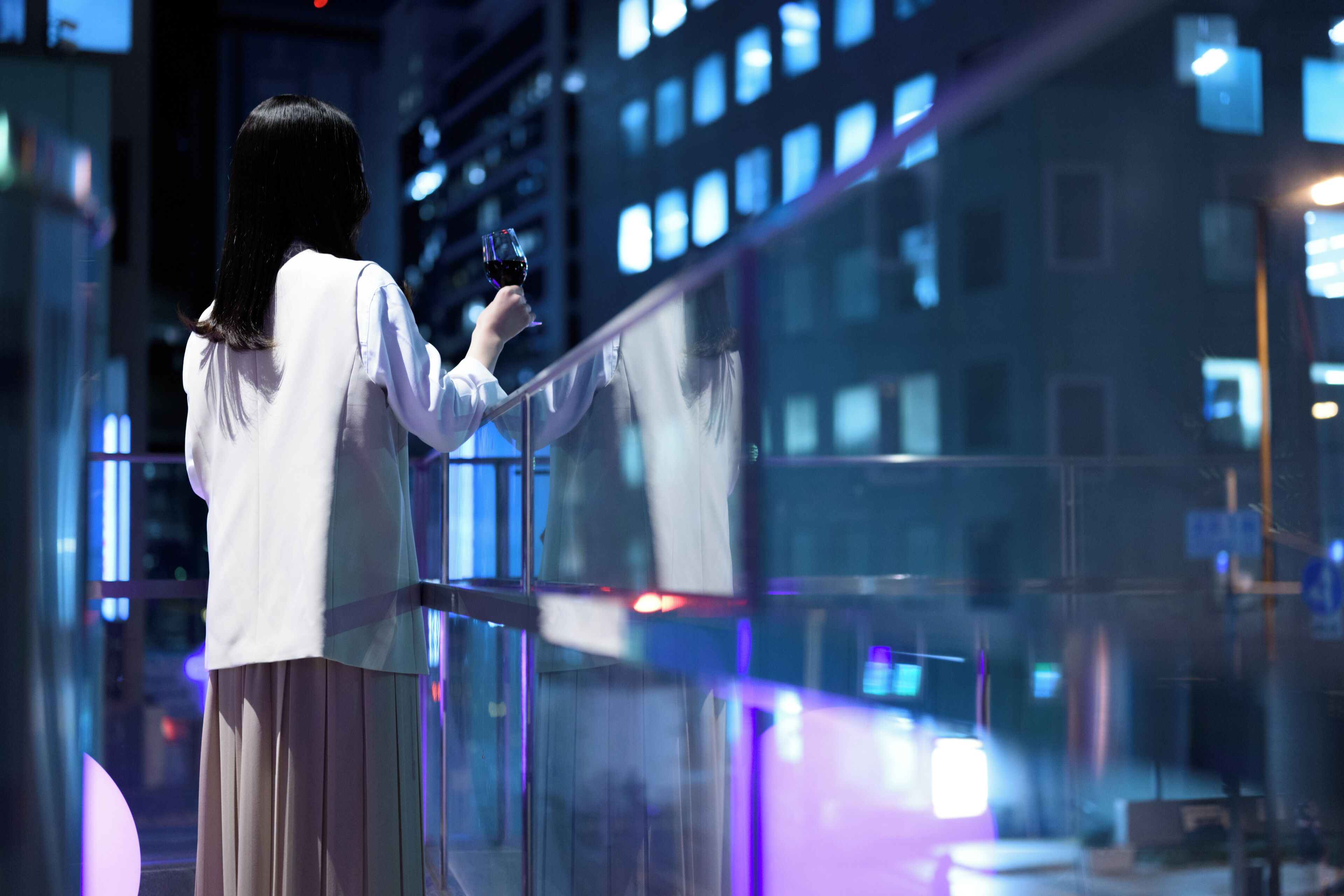A person holding a wine glass, standing by a glass railing with a cityscape in the background.
