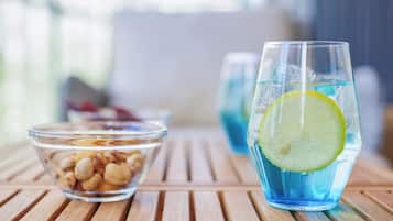 A glass of blue beverage with a lemon slice, a bowl of nuts, and a clear glass container on a wooden table.