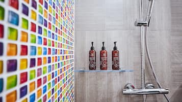 A bathroom with a tiled wall, a shower, and three bottles of shampoo and conditioner on a shelf.