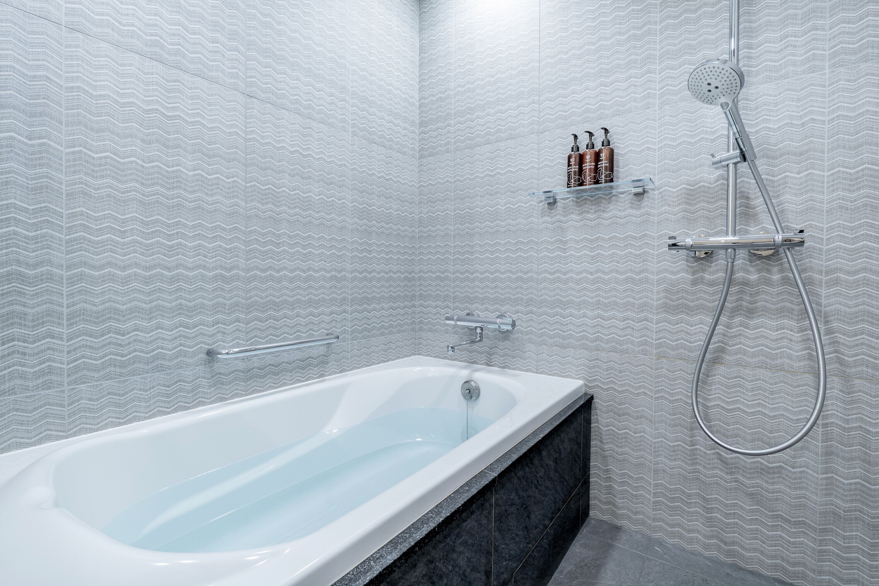Un baño moderno con una bañera independiente, ducha con cabezal de ducha manual y repisa con artículos de aseo.