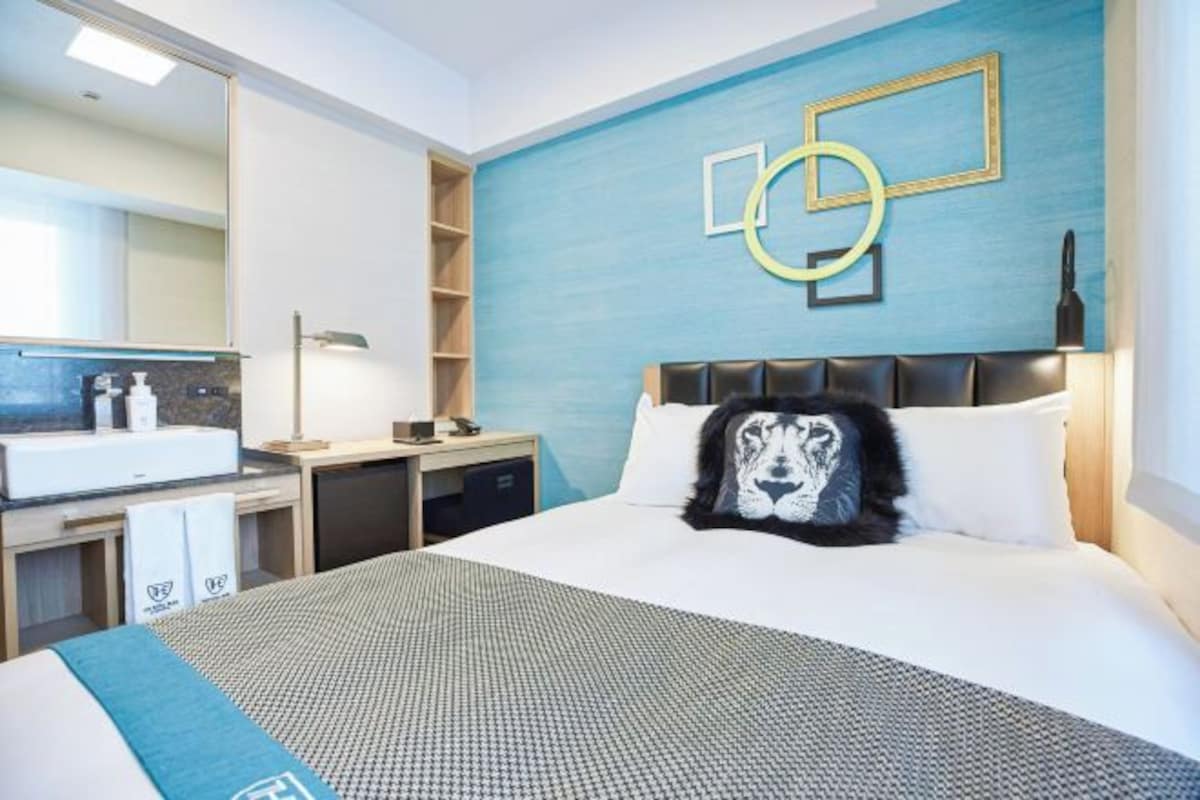 Habitación de hotel con una cama grande, cabecera con almohada con forma de perro, televisor montado en la pared, baño con espejo y lavamanos, y una pared de acento azul.
