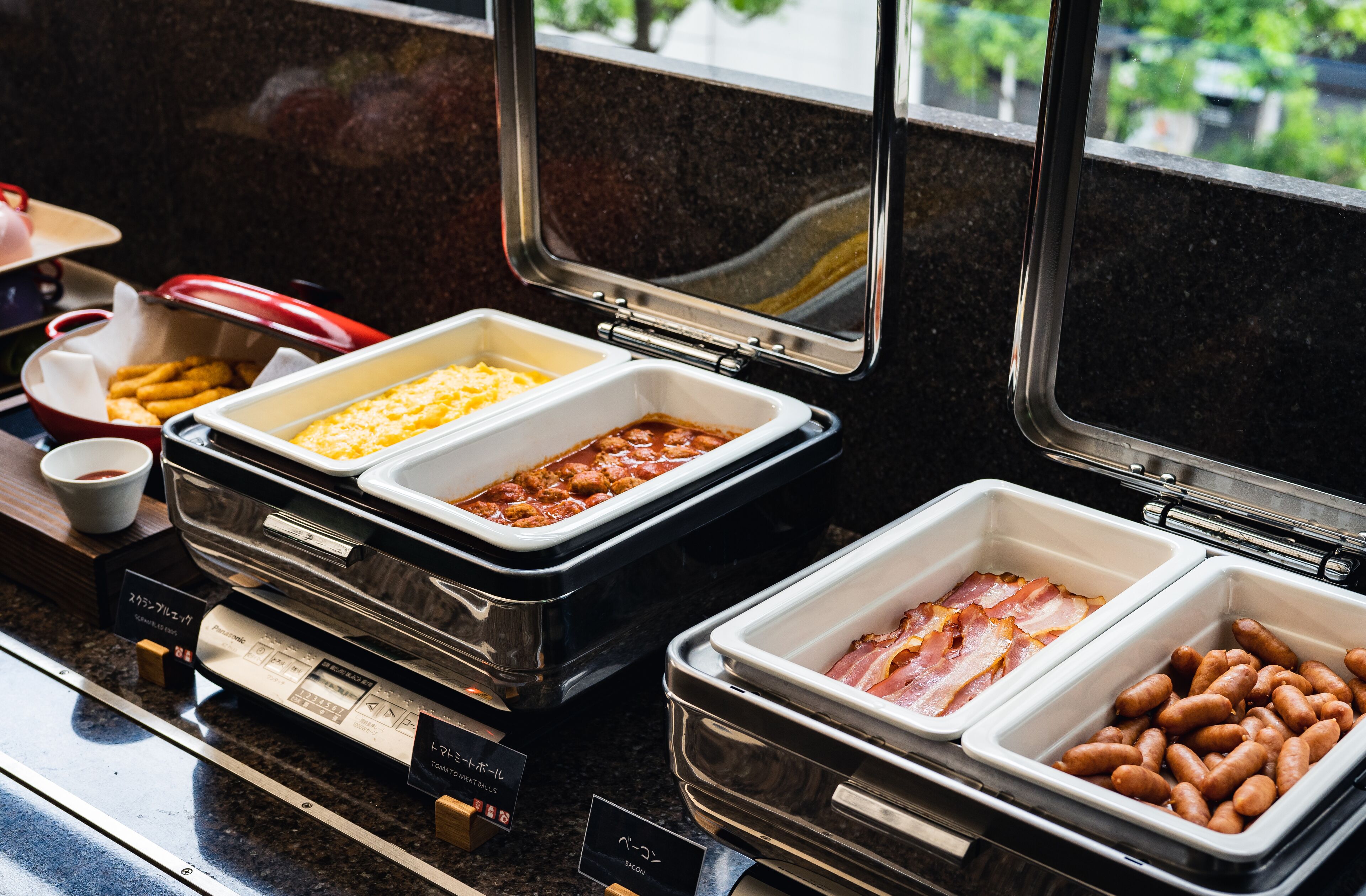 A buffet with various food options including beans, bacon, and a dish with a yellow sauce.