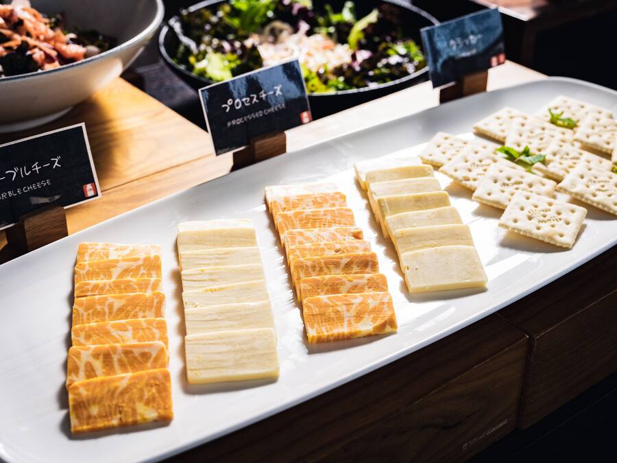 A variety of cheeses and crackers on a white plate, with labels indicating different types.