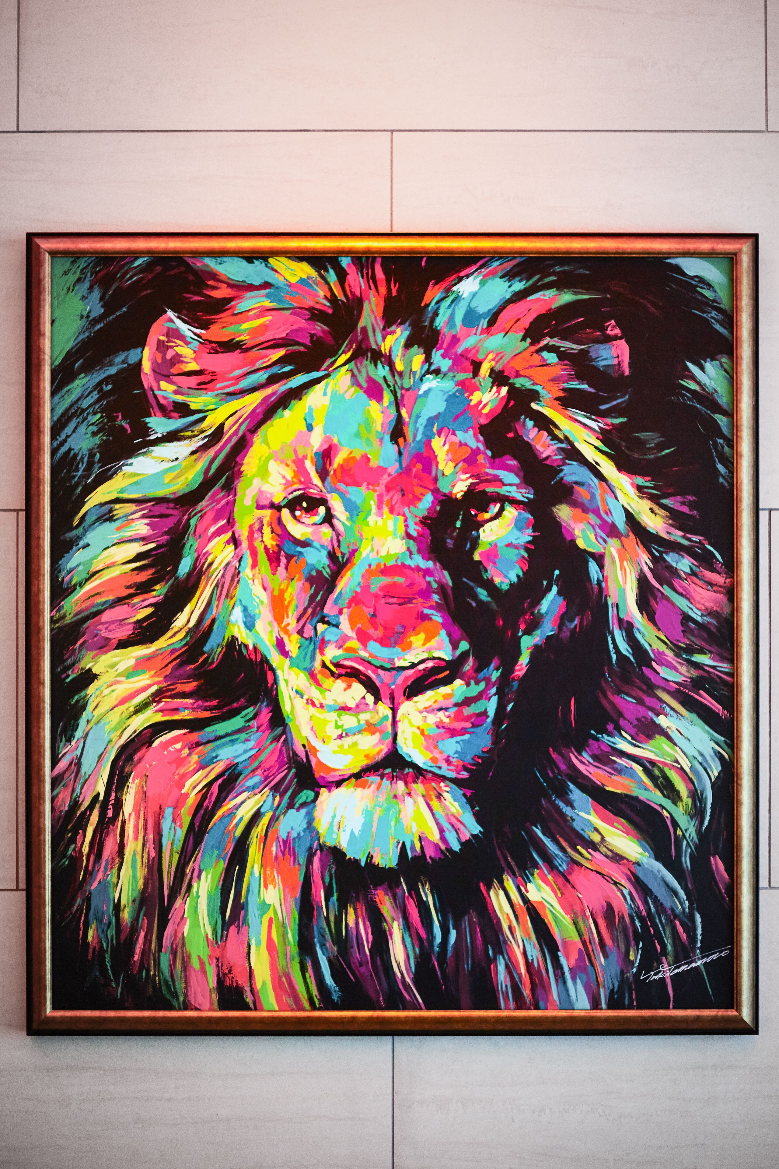 A framed painting of a lion's face with a colorful, abstract background.