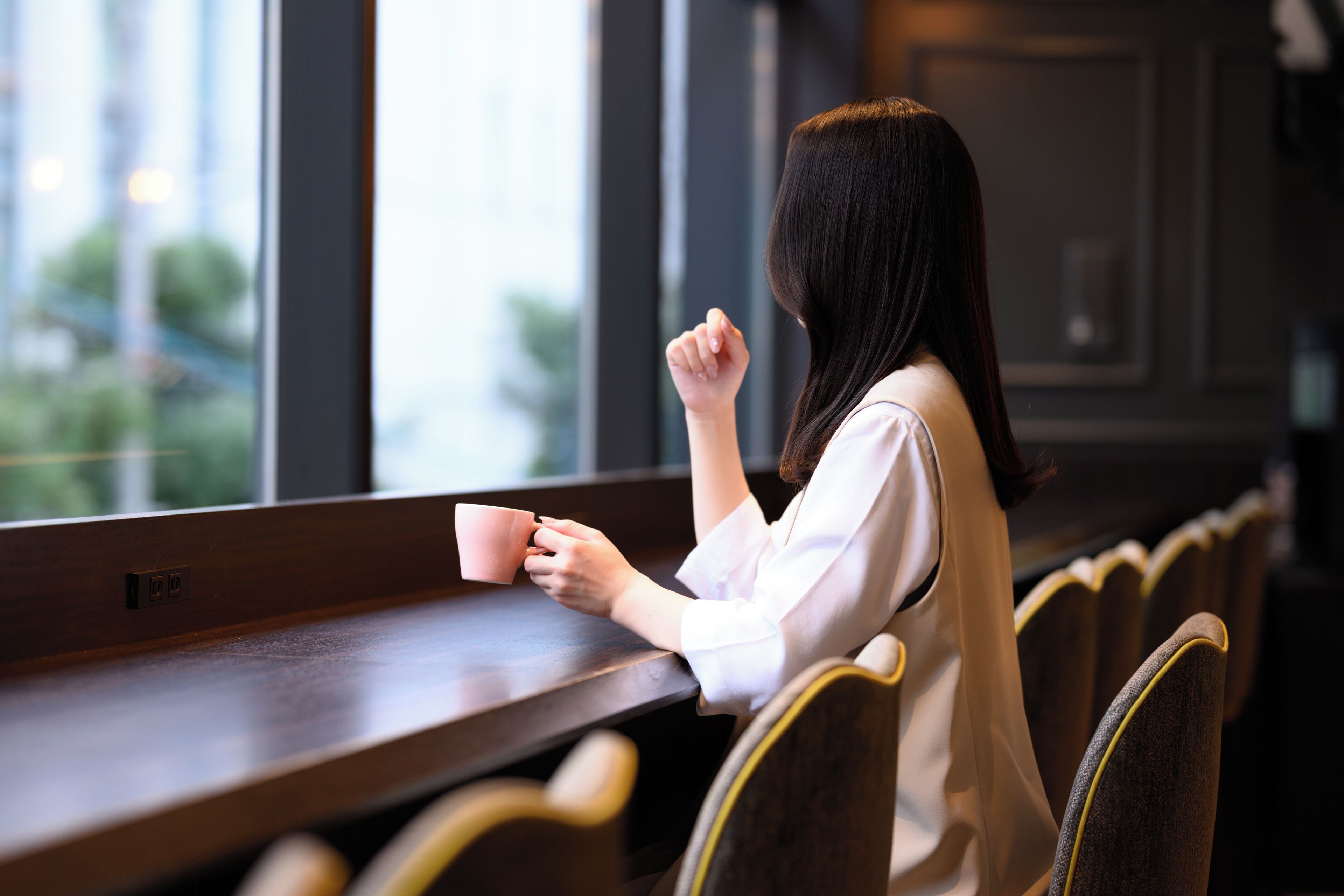 Une personne est assise à une table en bois, avec une fenêtre en arrière-plan.