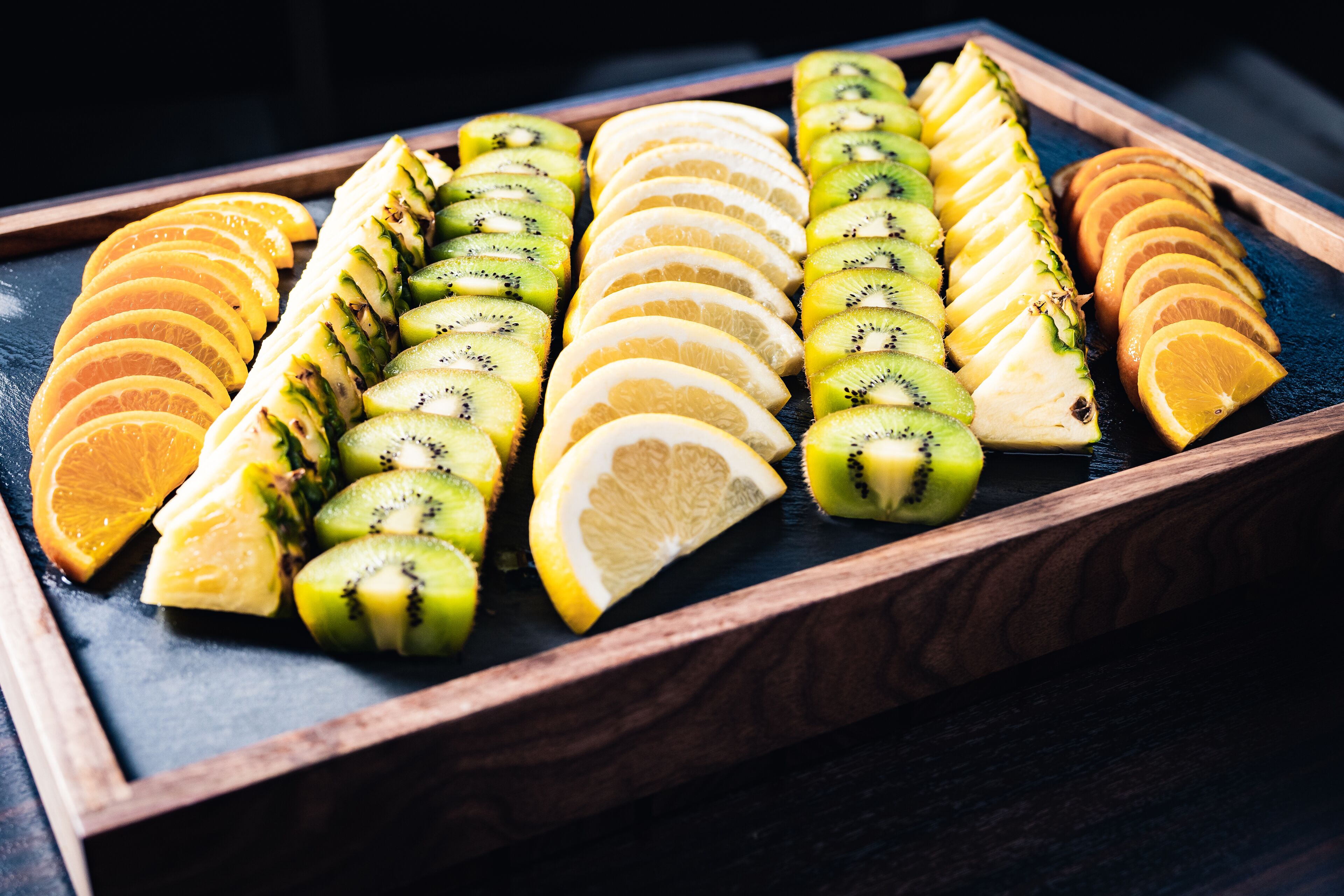 Een houten dienblad met netjes gerangschikte stukken fruit, zoals sinaasappels, citroenen en kiwis.