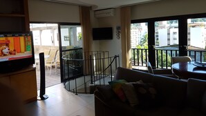 Een woonkamer met televisie, een bank, een eettafel en een balkon met een hekwerk.