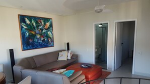Een moderne woonkamer met een bruine bank, een rode poef en een kleurrijk abstract schilderij.