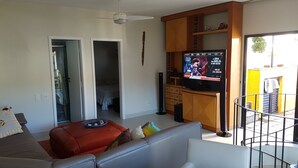 Een woonkamer met een bank, een televisie en een balkon.