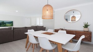 A modern living room with a white dining table, grey sofa, and a wooden cabinet. - Kay's Hideaway (Lennox Head)