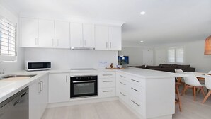 A modern kitchen with white cabinetry, a built-in oven, and a microwave. - Kay's Hideaway (Lennox Head)