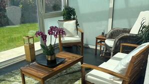 Un patio iluminado por el sol con un sofá de madera, una mesa de centro de madera y una pequeña mesa con una planta.