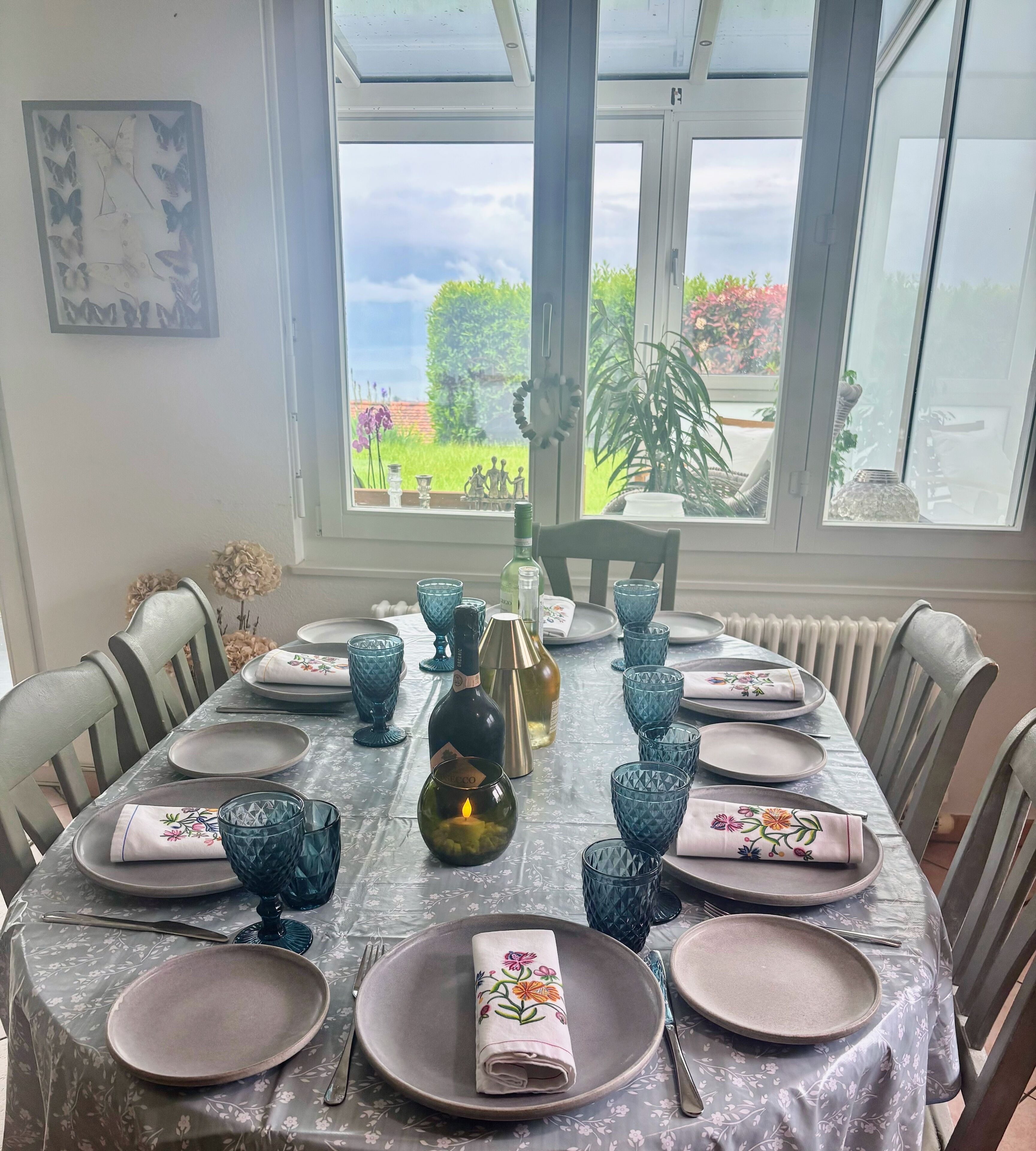 Mesa de comedor preparada para seis personas, con copas azules, una vela y una botella de vino.