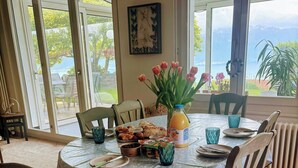 Comedor con mesa dispuesta para cuatro, mantel con estampado floral, una botella de jugo de naranja y un jarrón de tulipanes.