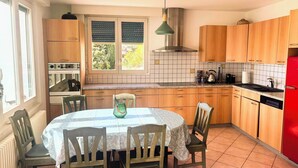 Una cocina con armarios de madera, una mesa de comedor con sillas, un refrigerador rojo y una ventana con persianas.