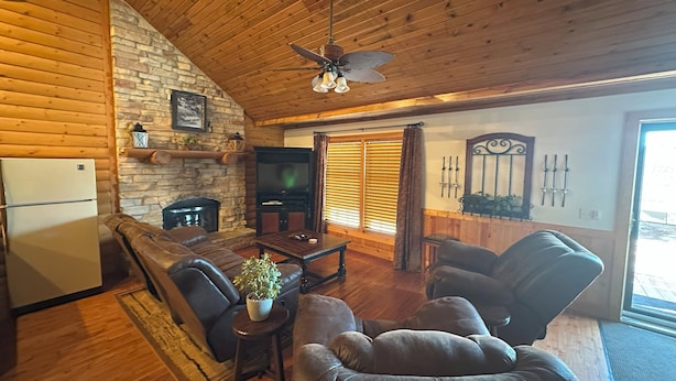 A cozy living room with a stone fireplace, wooden ceiling, and a large TV. - Apple Canyon Lake, Game Room, Hot Tub (Apple River)