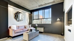 A modern living room with a sofa, coffee table, and a large window with a city view. - Roomy Loft near Guy-Concordia Metro (Montreal)