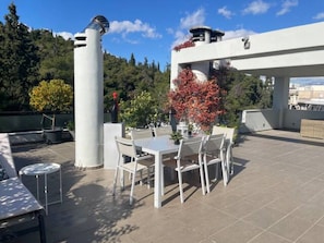 A rooftop terrace with a table and chairs, surrounded by a white structure and trees.