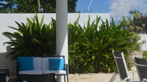 An outdoor patio with a glass-top table, white wicker chairs, a white sofa with blue cushions, and green plants. - Beautiful Garden Pool, Walk to Town   (Vieques)
