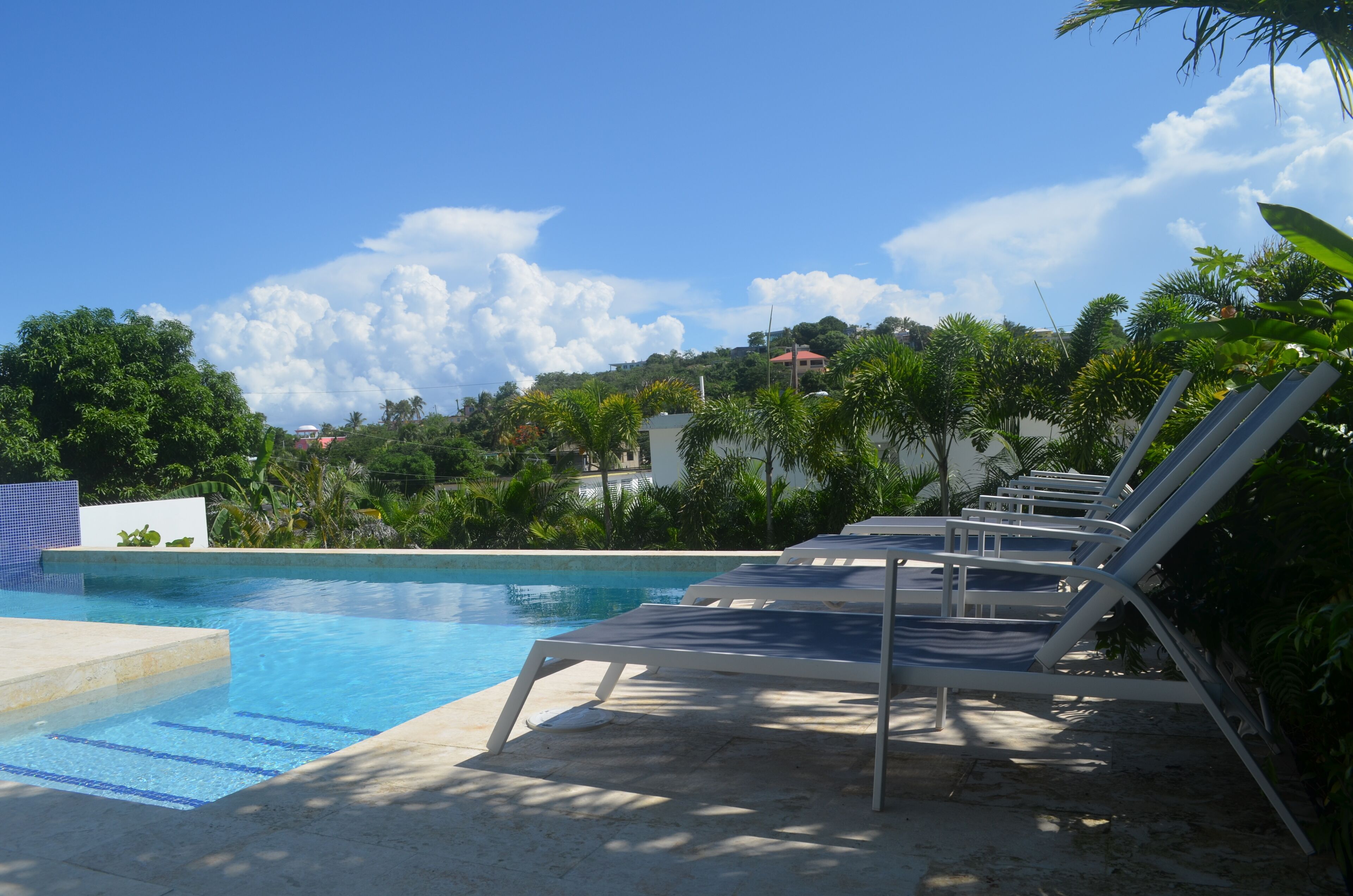 A swimming pool with lounge chairs and a view of a hill with buildings.