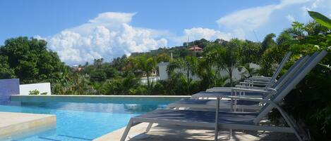 A swimming pool with lounge chairs and a view of a hill with buildings.